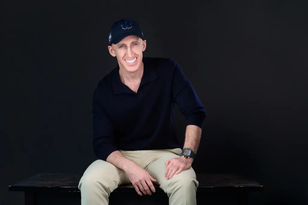 Uri Poliavich sitting in a dark studio wearing a black outfit and cap